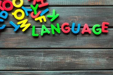 Learn foreign language. Concept with letters on dark wooden background top-down copy space