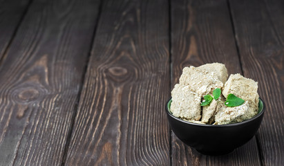Plate with sunflower halva decorated with mint leaves on a dark wooden table, selective focus. Copy space.