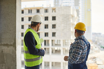 Two engineers discuss work related questions together holding folded blueprint.