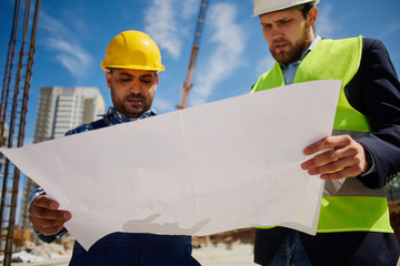 Close-up of a blueprint which two engineers examine.