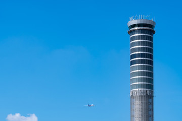 Air traffic control tower in the airport with international flight plane flying on clear blue sky....