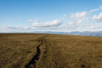 Fototapeta premium A mountain field with a very long crack going toward the horizon, beneath a deep blue sky with white clouds