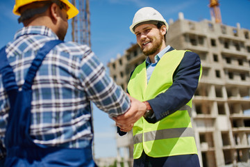 Two male engineers shake each others hands friendly.