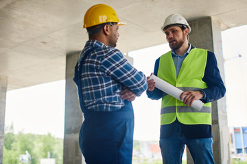 Two engineers discuss work related questions together holding folded blueprint.