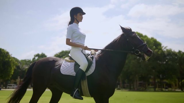 pretty girl in helmet and boots on bay horse pacing on horse arena, horse ride in the fresh air equestrian recreation activities