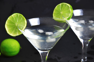 Two glasses of martini with lime on a black background. Two glasses of martini cocktail in a bar.