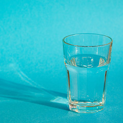A glass with clean clear clear water stands on a blue background with green shadows. Clean water