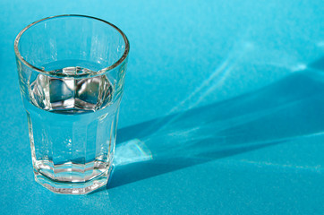 A glass with clean clear clear water stands on a blue background with green shadows. Clean water