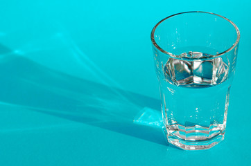 A glass with clean clear clear water stands on a blue background with green shadows. Clean water