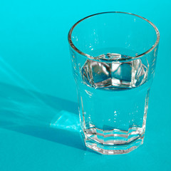 A glass with clean clear clear water stands on a blue background with green shadows. Clean water