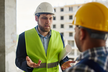 Two engineers discuss work related questions together holding folded blueprint.