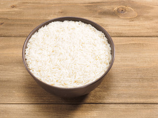 Long grain Basmati rice in brown ceramic bowl on brown wooden background