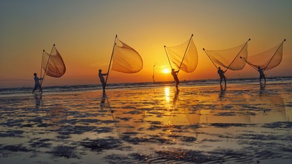 Fototapeta na wymiar Tan Thanh beach, Go Cong district, Tien Giang province, Vietnam - Feb 2020: Photo of fishing village people using homemade tools to catch fish in sea at sunrise