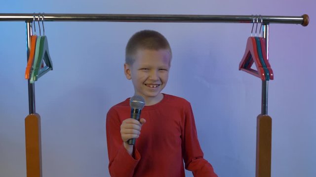 cute blond boy in red sweater at home. teenager climbed into dressing room took microphone and sings among empty hangers