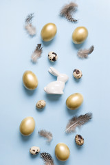 Easter decor of bunny, golden eggs, feathers on pastel blue. Top view. Happy Easter holiday. Greeting card. Vertical composition.