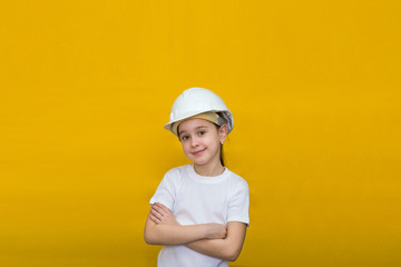 smiling little girl in a construction white helmet crossed her arms over her chest on a yellow background