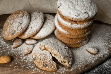 Oat cookies with pieces of chocolate, almond with powdered sugar. One cookie is broken in half.