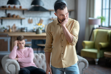 Man in orange shirt standing feeling bad after argument with his partner