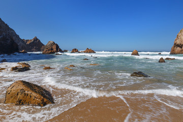 Scenic view of a waves, rocks and boulders and Atlantic ocean at the Praia da Ursa beach near Cabo da Roca, the westernmost point of mainland Europe, in Portugal.