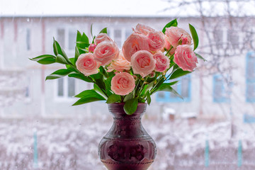Bouquet of spring roses in clay vase on window.