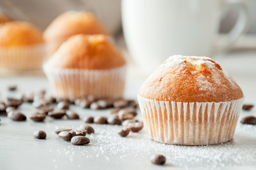 Fresh homemade tasty muffins ready to eat with are on a wooden table near a cup of coffee. Coffee beans are scattered on the surface of the table. Sweet dessert. Bon Appetit.