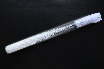 Test tube with ammonium nitrate in granular form, on a black background. The substance is one of the best mineral nitrogen fertilizers.