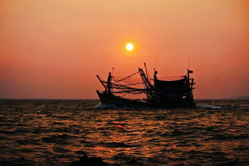The fishing boat returned to the shore at dawn with the sun.