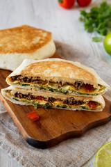 Tasty Homemade Beef Crunchwrap Quesadilla on a rustic wooden board, side view. Close-up.