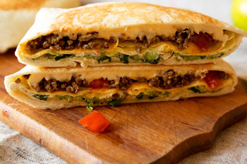 Tasty Homemade Beef Crunchwrap Quesadilla on a rustic wooden board, low angle view. Close-up.