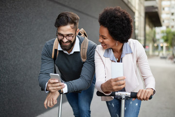 Happy business people going to work with electric scooter on urban street