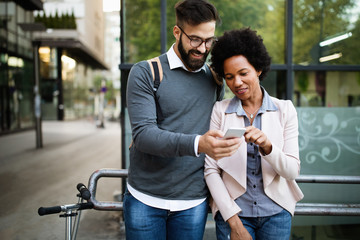 Happy businesspeople using technology devices gadgets near wall of modern building