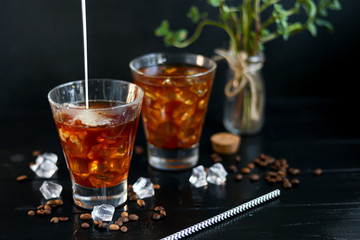 Iced coffee in a tall glass with milk and pieces of ice. On a dark background.