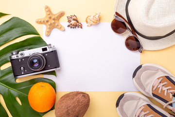Summer vacation background. Blank paper, monstera leaf, retro camera, sneakers, sunglasses and exotic fruits on yellow background