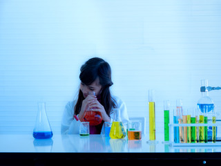 Cute little girl looking into Erlenmayer flask to see orange color formula. School lab with...