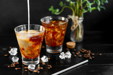 Iced coffee in a tall glass with milk and pieces of ice. On a dark background.
