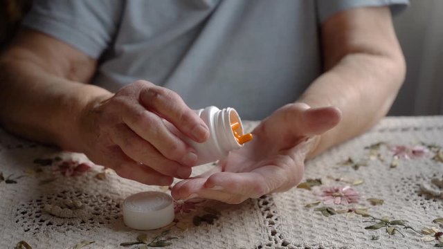 Slow motion shot of the old lady take orange pills from the white pillbox, senior lady hands, retired people health care