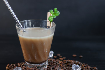 Iced coffee in a tall glass with milk and pieces of ice. On a dark background.