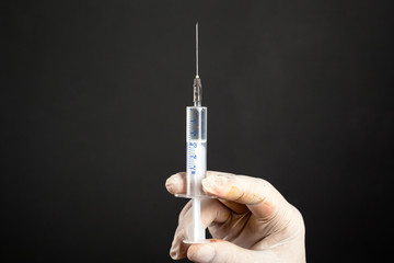 hand in a disposable sterile white glove holding a medical syringe 5 ml on a dark background close-up. shot an injection treatment