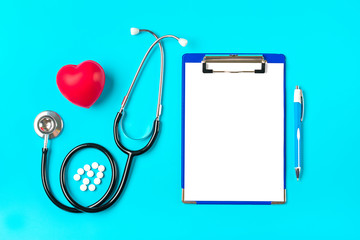 Phonendoscope, heart, tablet with white paper, pen, medicine on blue background Health, life,...