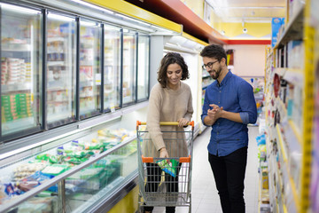 Smiling couple buying products in grocery store. Happy young man and woman with shopping trolley...