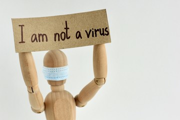 Cardboard sign with text I am not a virus in the hands of a wooden doll or mannequin in a medical...