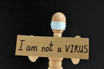 Cardboard sign with text I am not a virus in the hands of a wooden doll or mannequin in a medical mask. Concept of anti racism, anti xenophobia, the social situation around the Coronavirus or Covid-19