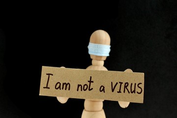 Cardboard sign with text I am not a virus in the hands of a wooden doll or mannequin in a medical mask. Concept of anti racism, anti xenophobia, the social situation around the Coronavirus or Covid-19