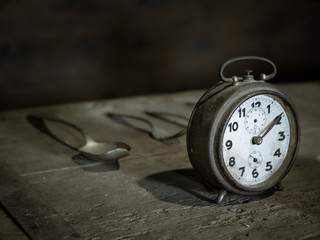 Reloj antiguo con cubiertos encima de mesa de madera deteriorada.