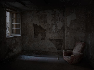 Habitación abandonada en penumbra con sofá y ventana abierta.