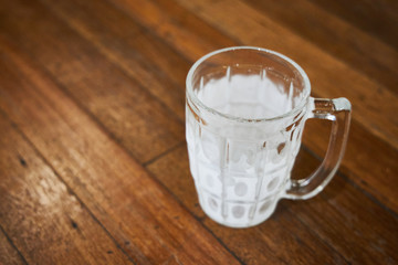 An empty mug for beer covered with hoarfrost stands on a wooden table of a pub