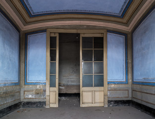 Puerta acristalada de entrada de habitación azul con cenefas de casa abandonada.