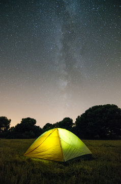 Tienda de campa&ntilde;a de noche en medio del campo y fondo de estrellas y la v&iacute;a l&aacute;ctea de fondo.