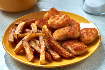 Tasty homemade potato french fries with chiken nuggets on yellow dish