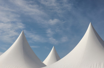 A row of white triangular pyramid marquee rooftops against a blue sky